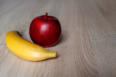 Fresh red apple and ripe yellow banana on wooden table, healthy fruits close-up with copy spaceの写真素材