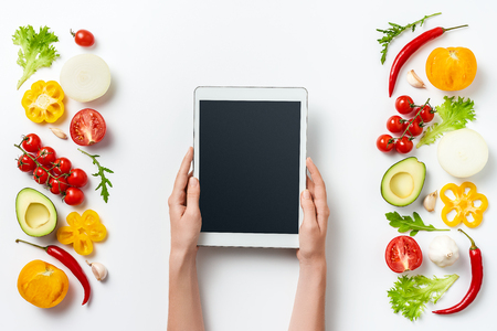 digital tablet in woman hands and herbs and vegetables isolated on white background. Copy space. Healthy eating background. Food photography. Top viewの写真素材