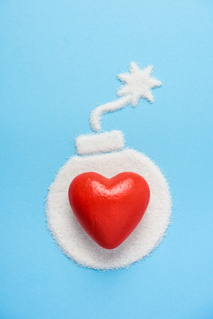 Big red heart on the bomb made of sugar on blue blue background. Diabetes concept. Sugar Kills. Suggesting dieting concept. Unhealthy white sugar concept. Copy space. Space for text.の写真素材