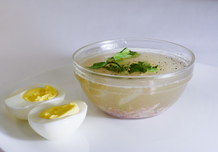 a glass bowl of broth with egg and greensの写真素材