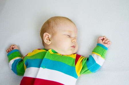 baby in striped suit lying on a light blanketの写真素材