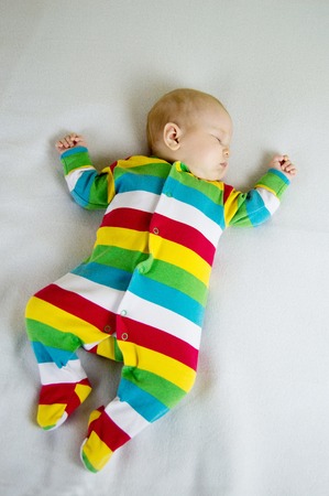 baby in striped suit lying on a light blanketの写真素材
