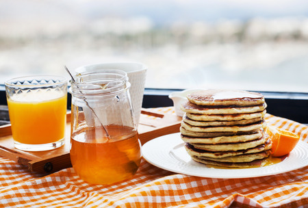 Breakfast with pancakes, coffee, honey and juice on table at the window