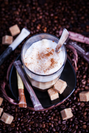 Glass of fresh hot tasty latte macchiato on coffee beans and sugar background, dark styleの写真素材