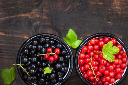 Fresh delicious organic red and black currants in a mugs on wooden tableの写真素材