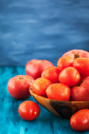 Fresh ripe wet red tomatoes in wooden bowlの写真素材