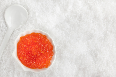 Delicious red caviar in bowl on white snow background, top viewの写真素材