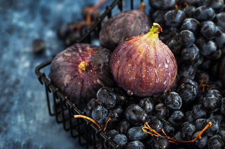 Fresh figs and purple grape in basket on dark wooden backgroundの写真素材