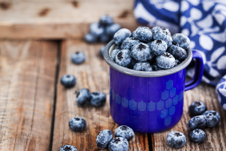 Fresh ripe blueberries and in blue enamel mug on rustic backgroundの写真素材