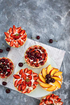 Fresh delicious cherry, strawberry and peach tartlets on gray backgroundの写真素材