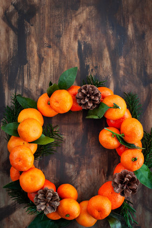 Wreath of fresh ripe tangerines with leaves and cones, on wooden background, top view, copy space, holiday decorationの写真素材
