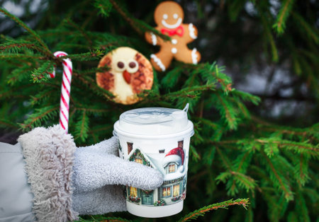 Woman`s hand hold a cup of coffee on Christmas cookies and fir-tree background, outdoor