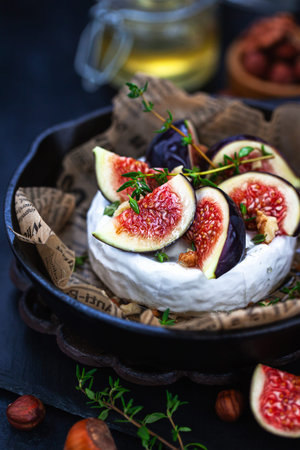 Camembert or brie cheese with fresh figs walnuts  and honey on iron frying pan, over dark backgroundの写真素材