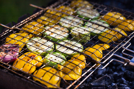 Grilled vegetables (zucchini and bell pepper) on barbecue, green grass background, summer outdoorの写真素材
