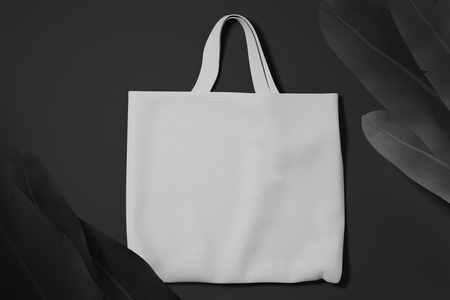 White cotton bag on black matte background with tropical flowers. Top view. Mock up.の写真素材
