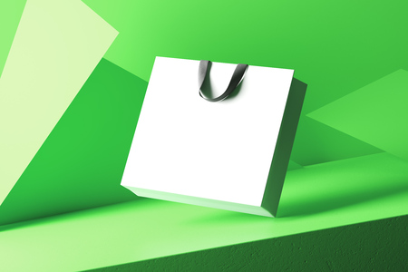 White paper shopping bag with black handles isolated on green geometric background.の写真素材