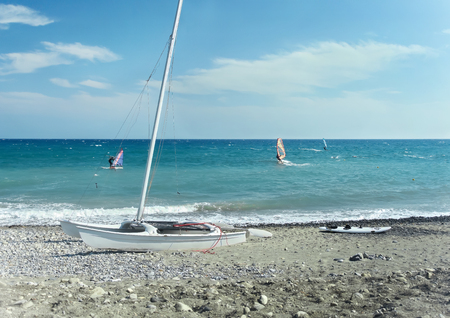 Windsurfing in the Ligurian Sea and lonely yacht on the beachの写真素材