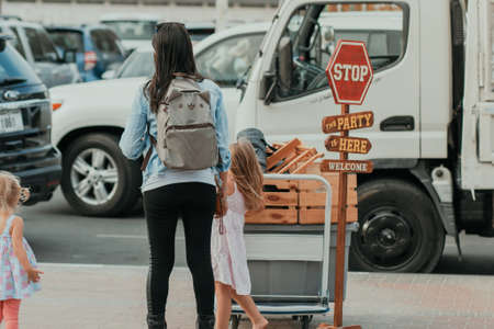 Mom with backpack with kids on the parking looking and waiting for a car to pick their luggage and baggage up with many vehicles on the backgroundのeditorial素材