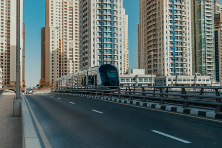 Modern tram navigating through pedestrian crosswalk bridge above promenade marina water with...