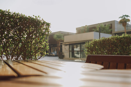 Empty wooden table and chairs at an outdoor cafÃ© with a view of surrounding greenery and buildingsの写真素材