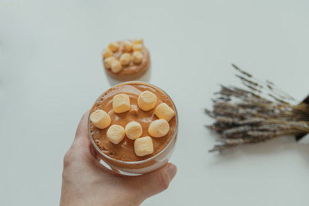 Holding homemade dalgona delicious drink coffee in hand with marshmallows, whipped sugary coffee on...