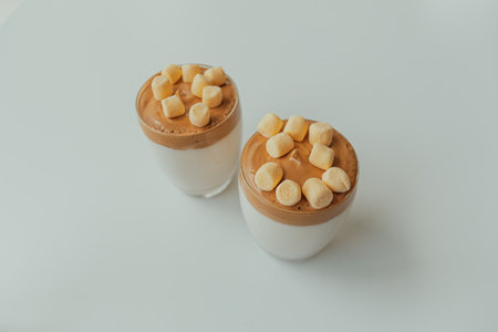 Two gourmet dalgona coffee drinks with marshmallows topping, whipped coffee and milk on white...