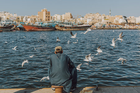Dubai, UAE - January 6, 2020: Man enjoying waterfront view with boats and seagulls in Dubai Creekのeditorial素材