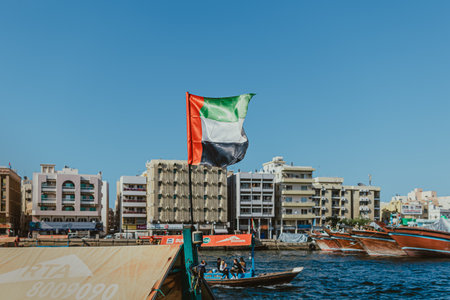 Dubai, UAE - January 6, 2020: UAE flag waving near Dubai Creek with city buildings in the backgroundのeditorial素材