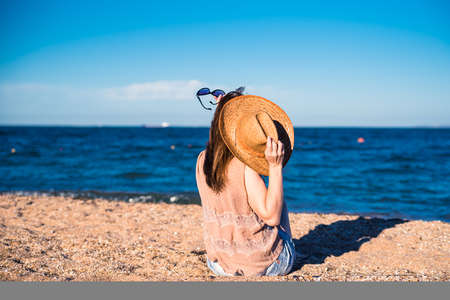 The girl sits with her back to us, and in front of her is the sea / ocean / water. Nice view with the girl.の写真素材