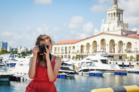 Sochi, Russia, July 27, 2019: a girl in a red photograph looks at us through the camera nikon, behind her back sochi port summer timeのeditorial素材