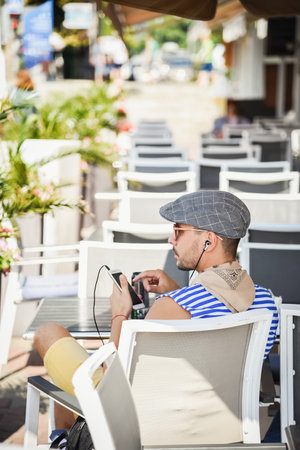 Sochi, Russia, July 27, 2019: traveler man sits with his back in a cafe on the pier, listens to music on a smartphone and looks away Sochi. summer timeのeditorial素材