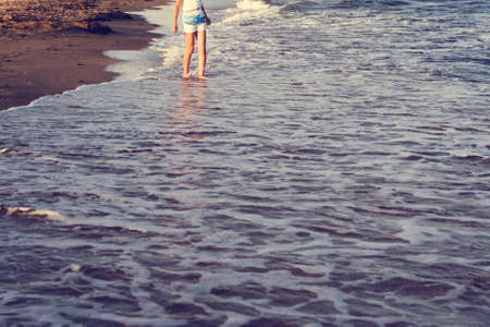 Cute little girl running through water at the beach, child enters the sea wave, summer vacation,...