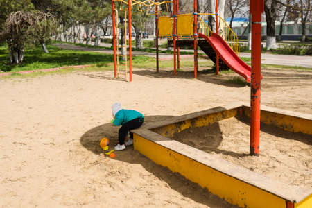one little girl playing in sand on outdoor playground. april warm day baby outdoors plays games