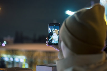 Selective focus on smartphone screen recording, blogger influencer on couch streaming live, a young woman in a hat on the street in winter makes a video call or broadcastの写真素材