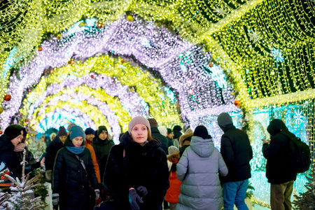 a woman in a knitted hat and fur coat in Christmas decorated with holiday lights. New Year's Eve, festive atmosphere. Moscow, Tverskoy Boulevard. Spending winter time outdoors. Warm clothes, knitted hat, mittensの写真素材