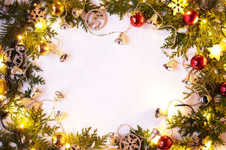 Christmas or New Year background: fir branches on a white background with wooden toys and a sparkling garland, bells, balls. White frame for congratulationsの写真素材