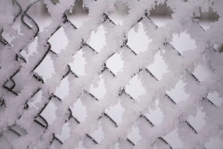 Snowy frozen metal fence close-up.Winter snowy weather.Old rural fence with smaller holes covered with snow.Cloudy cold day.Winter freezing scenery,low temperatureの写真素材
