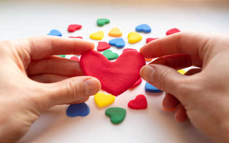 Hands holding red valentines on valentine's day. The girl's hands hold a lot of small hearts and fast-setting plasticine. The 14th of February. Holiday love. The concept of giving loveの写真素材