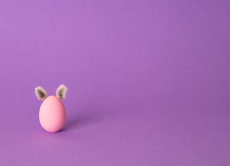 Row of colorful Easter eggs with willow bud ears painted in simple colors on a light purple...