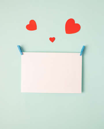 Greeting card concept for valentines day, wedding or mothers day, womens day. blank sheet of paper and beautiful red cute paper hearts on blue, mint background, top viewの写真素材