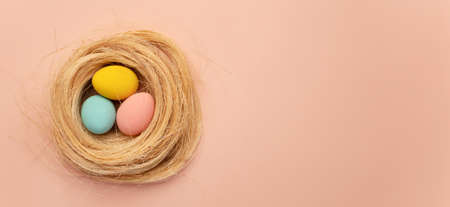 happy easter card. colored yellow, pink, blue easter eggs on a beige nest background from above,...