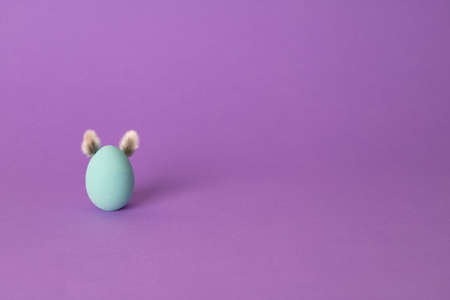 Row of colorful Easter eggs with willow bud ears painted in simple colors on a light purple background - side view with copy spaceの写真素材
