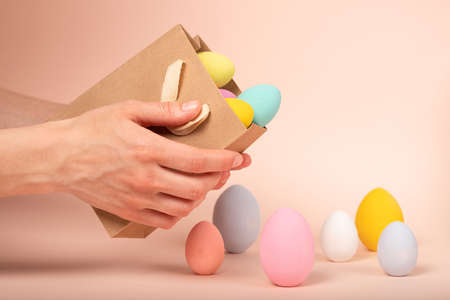 Women's hands pour out multi-colored Easter eggs from a shopping bag. Online shopping for the holidays. Symbols, traditions concept. Wide banner on a beige background. home delivery.の写真素材