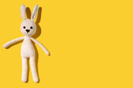 White amigurumi hare lies on a yellow background. Needlework concept. There is a place for text. Cope space. Happy easter.の写真素材
