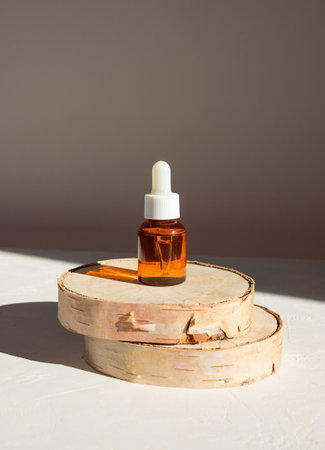 Mockup cosmetic face serum brown glass bottle with a pipette on a stylish minimalist beige white background wooden pedestal. Shadow from a sun. Female beauty concept, empty templateの写真素材