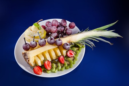 Fresh fruit salad served with fresh pineapple, pear, grapes, kiwi, strawberries, dusted with icing sugarの写真素材