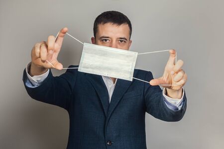 European man holds a medical mask at arms length in front of his face.の写真素材