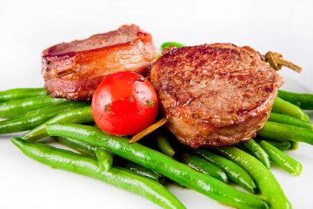 Fried pork medallions on skewers with string beans and one whole tomato.の写真素材