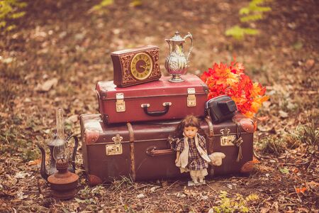 Antique suitcases, watches, doll, kerosene lamp, jugs, autumn leaves, photo camera in a case in park. Autumn vintage decor for an open air photo shoot.の写真素材