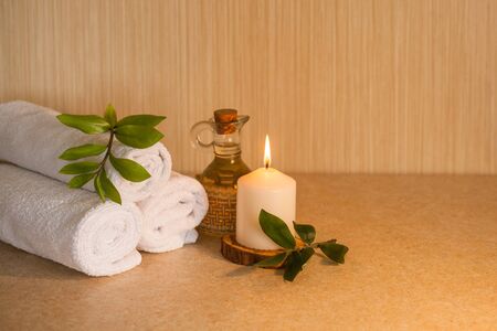 Towels, cosmetic massage oil, leaves and burning candle on a wooden stand. Spa, beauty and wellness concept.の写真素材